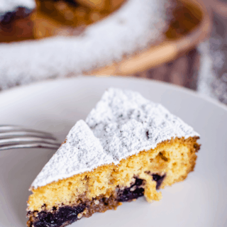 overhead photo of slice of cherry cake with icing sugar on a white plate and fork