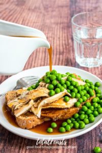 Gravy pouring on hot turkey sandwich with peas and glass of water in background