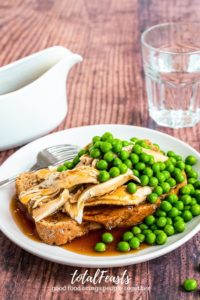 hot turkey open sandwich on white plate and gravy and peas