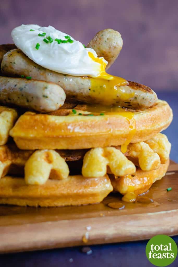 side shot of savoury southern cornmeal waffle stack with sausages and a poached egg